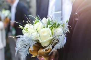 pexels-photo-306176-306176 Close-up of a white rose bouquet held by a groom at an outdoor wedding ceremony.
